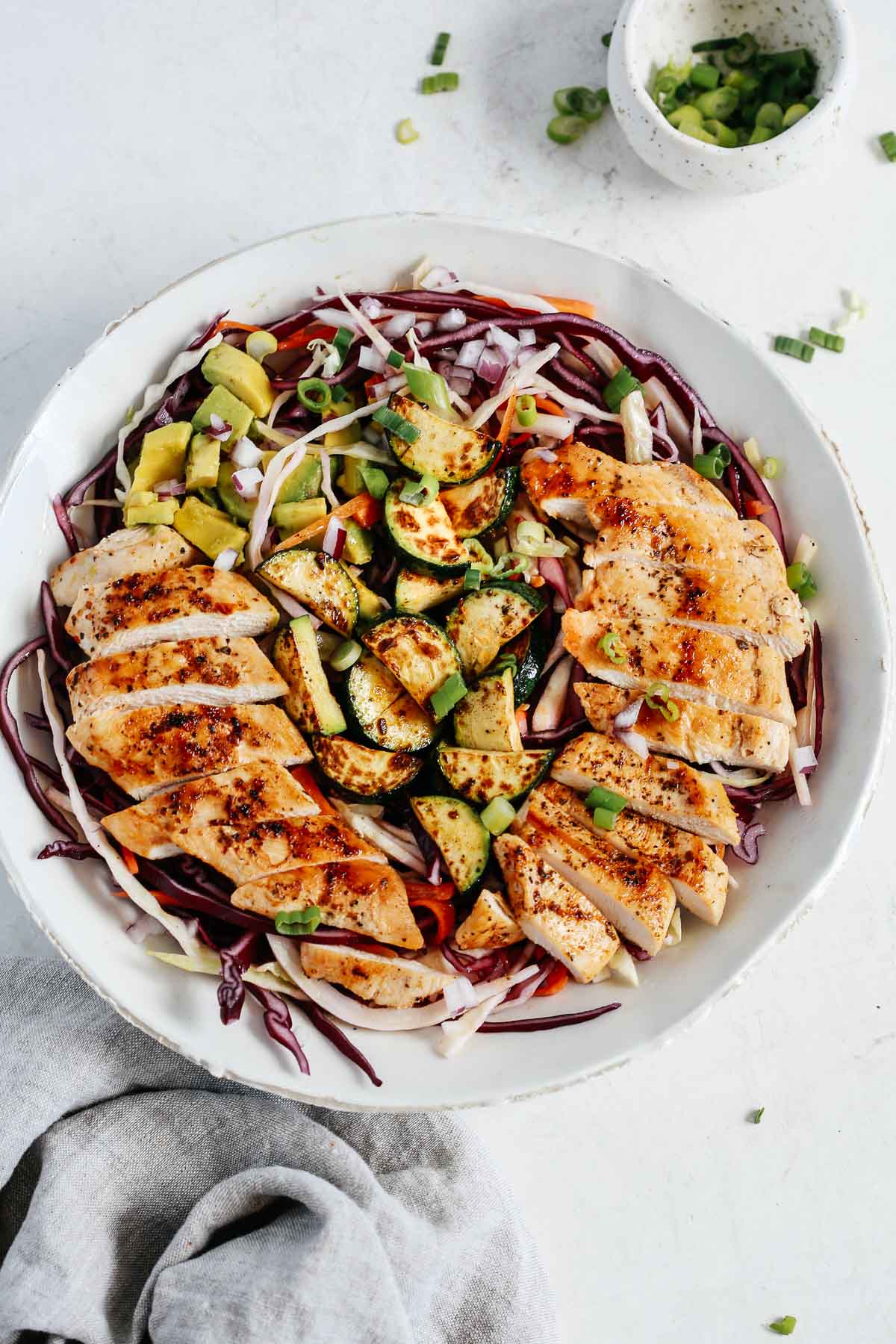 overhead view of a cabbage salad with chicken, zucchini, and avocado in a white bowl