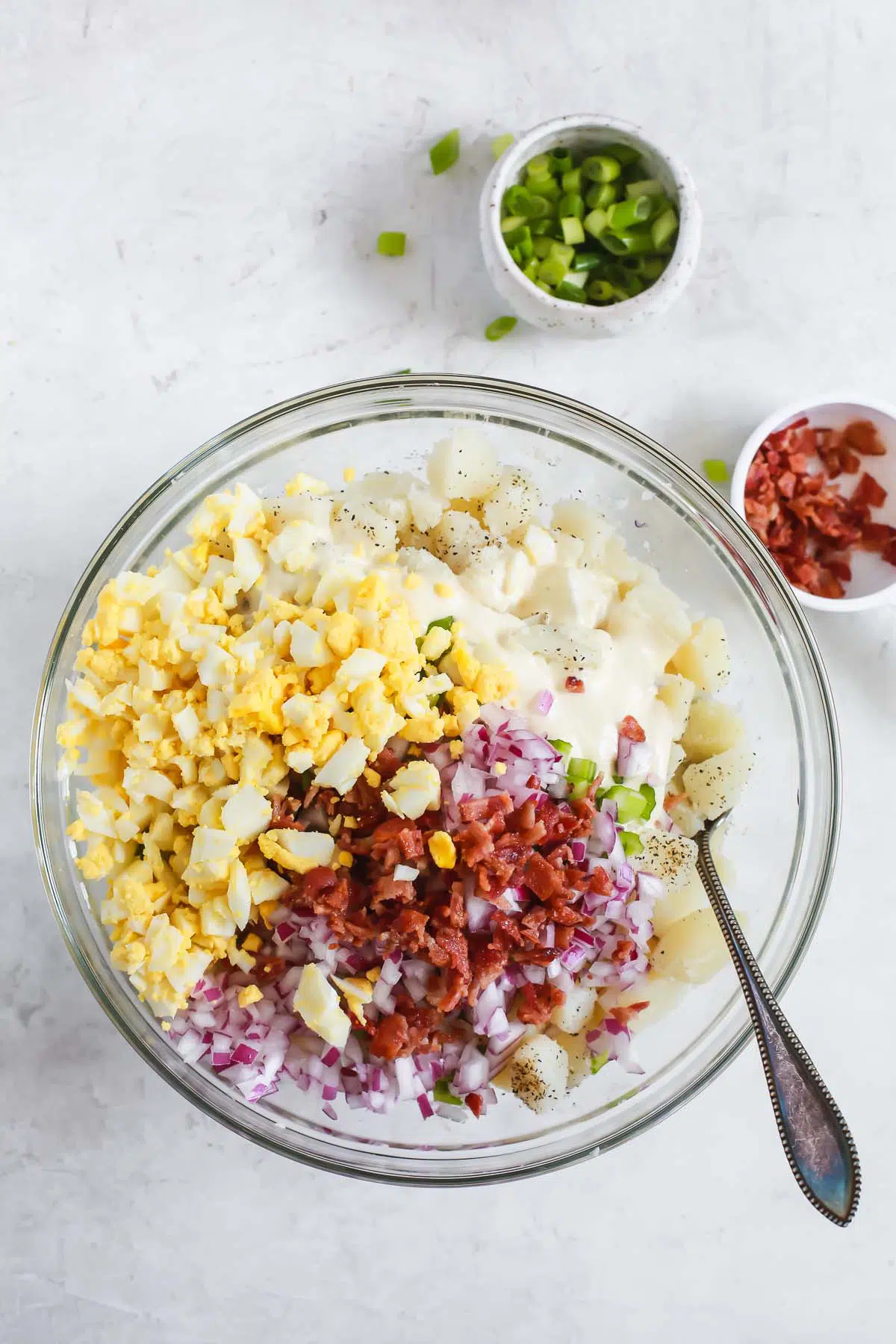 combining mayonnaise, eggs, potatoes, and bacon bits in a bowl