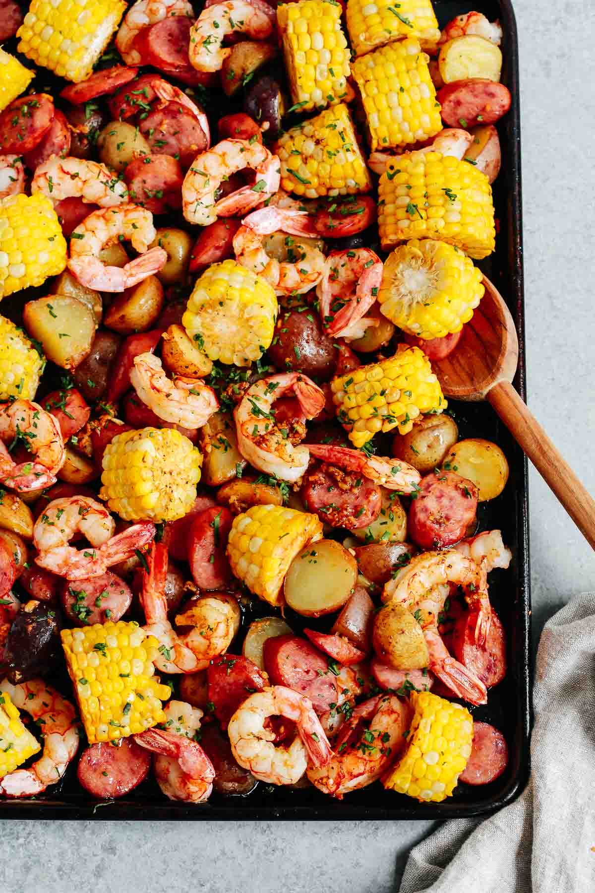 cooked shrimp dinner on a sheet pan with wooden spoon