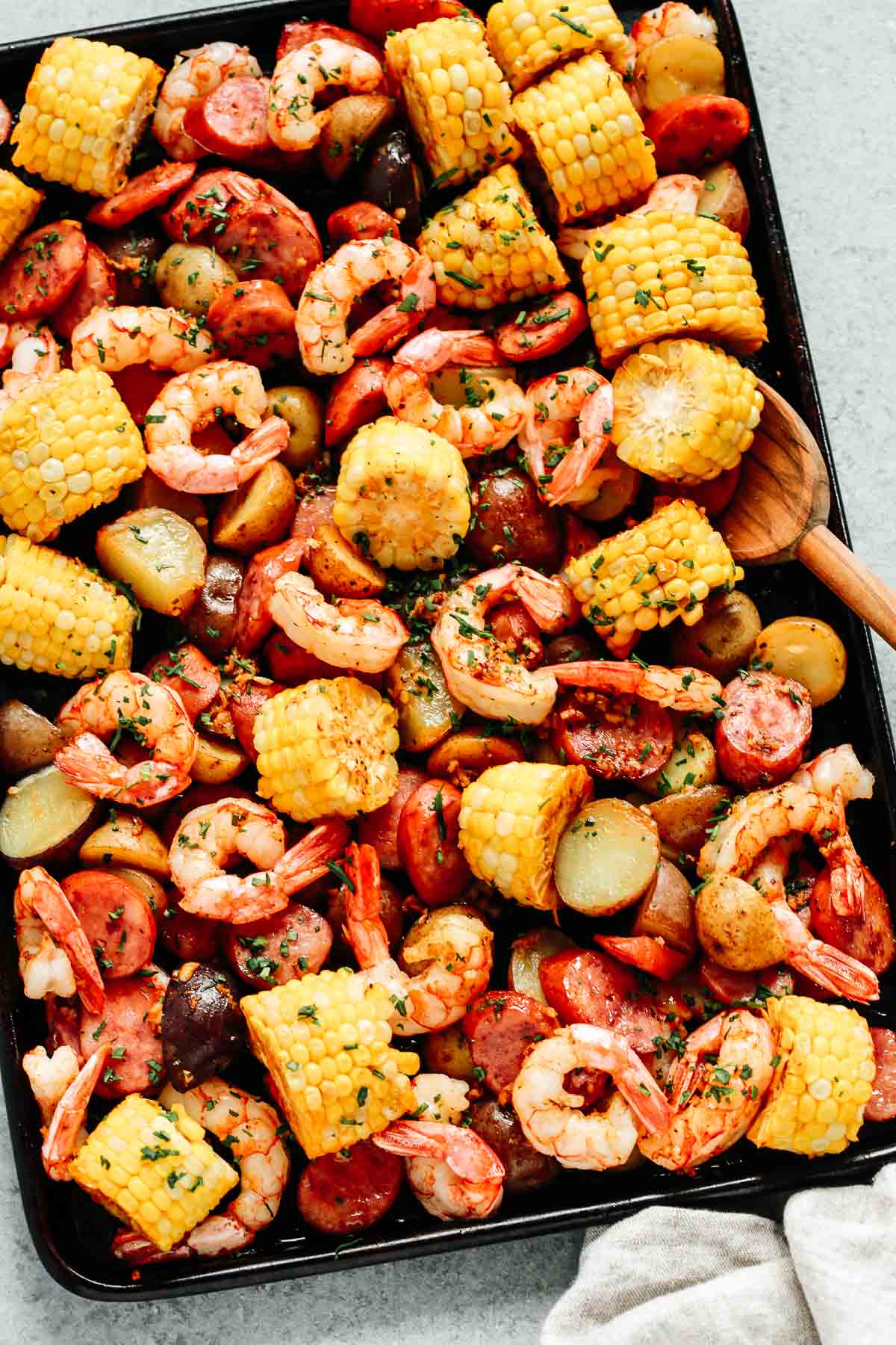 Sheet pan with shrimp boil with a wooden spoon.