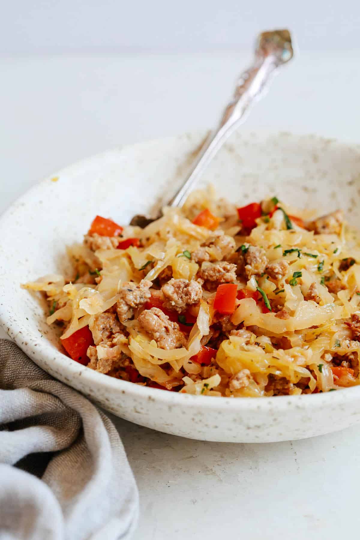close up of a metal fork in bowl filled with cooked cabbage, sausage, and bell peppers