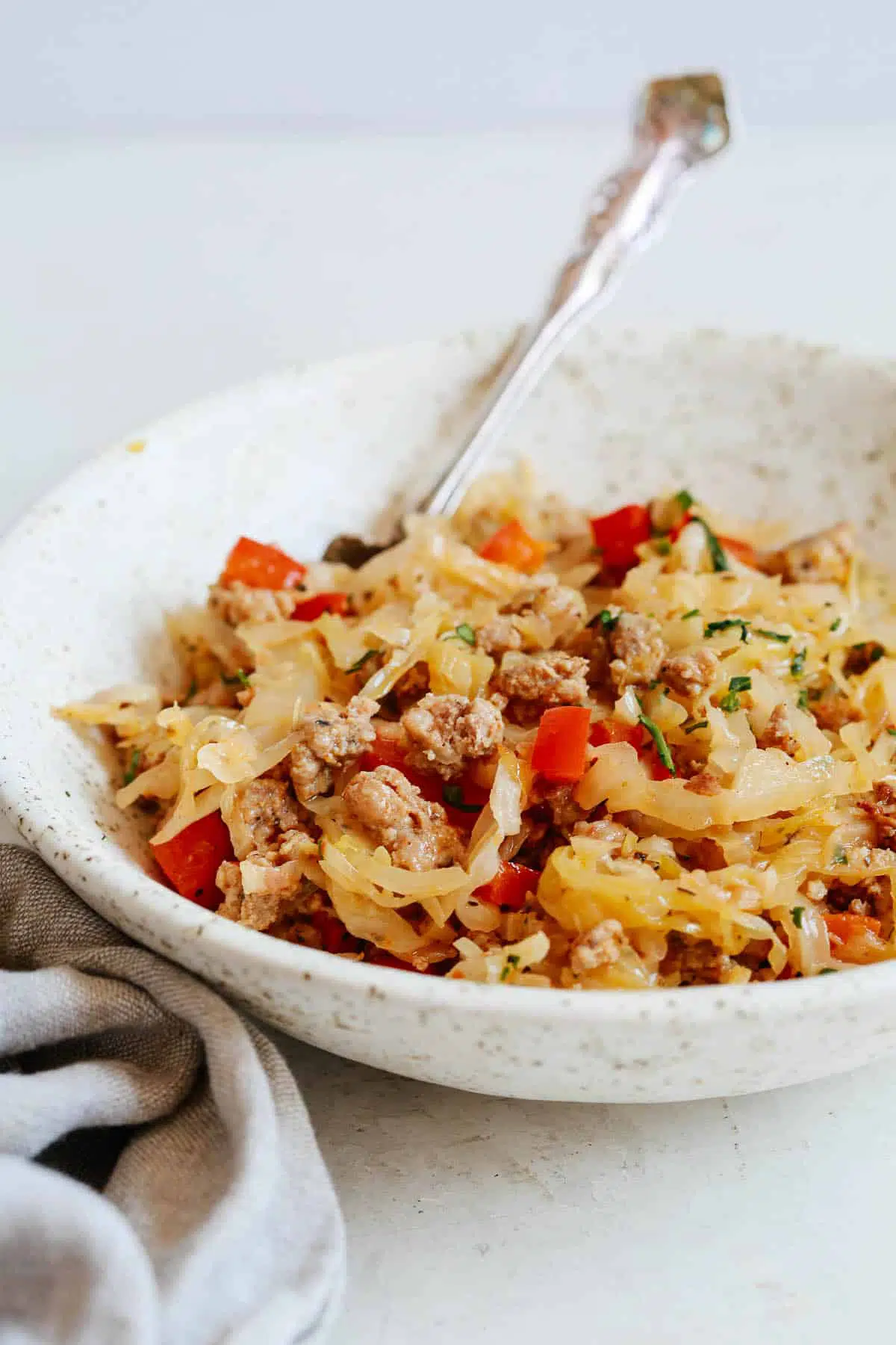 close up of a metal fork in bowl filled with cooked cabbage, sausage, and bell peppers 