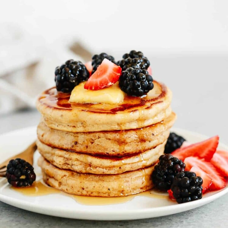 stack of gluten free pancakes topped with syrup and berries on a white plate