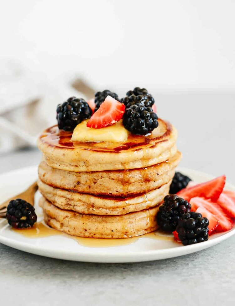 stack of gluten free pancakes topped with syrup and berries on a white plate