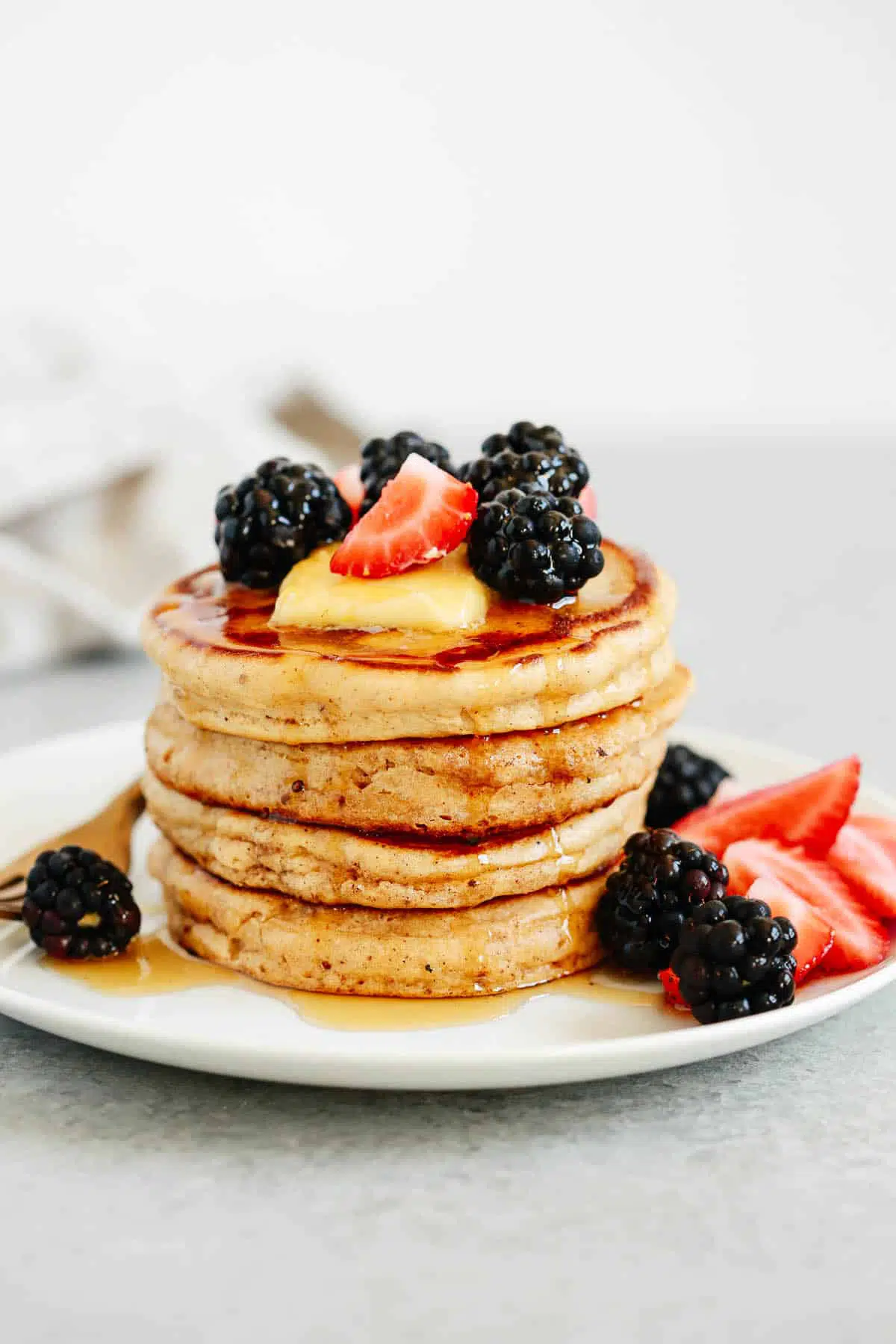 stack of gluten free pancakes topped with syrup and berries on a white plate 