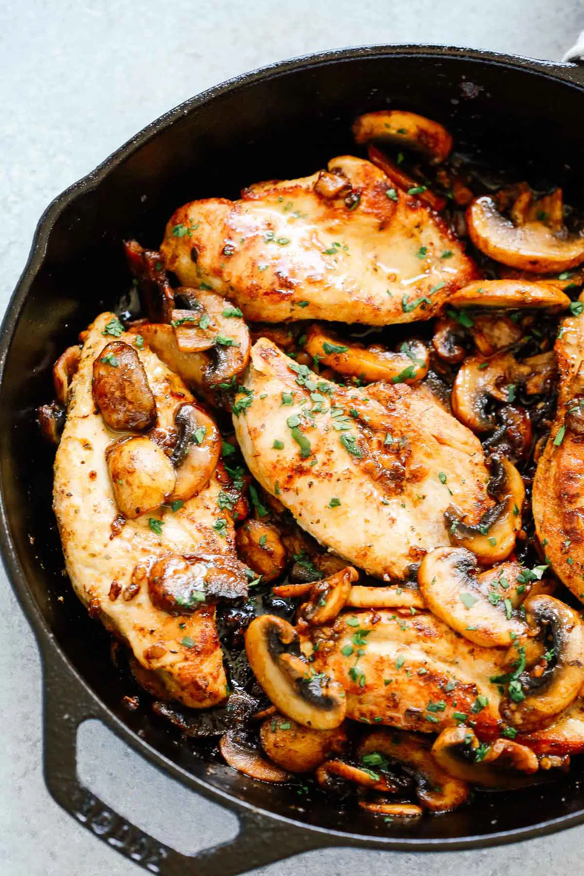 close up of mushrooms and chicken breast topped with fresh parsley in a skillet