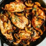 overhead photo of cooked chicken breasts and mushrooms in a cast iron skillet