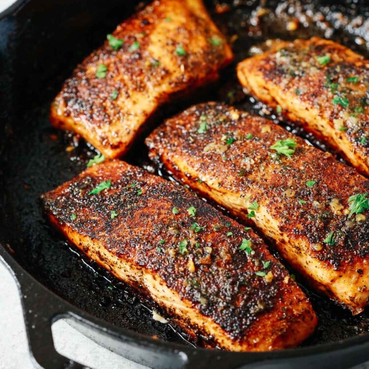 four blackened salmon fillets in a cast iron skillet