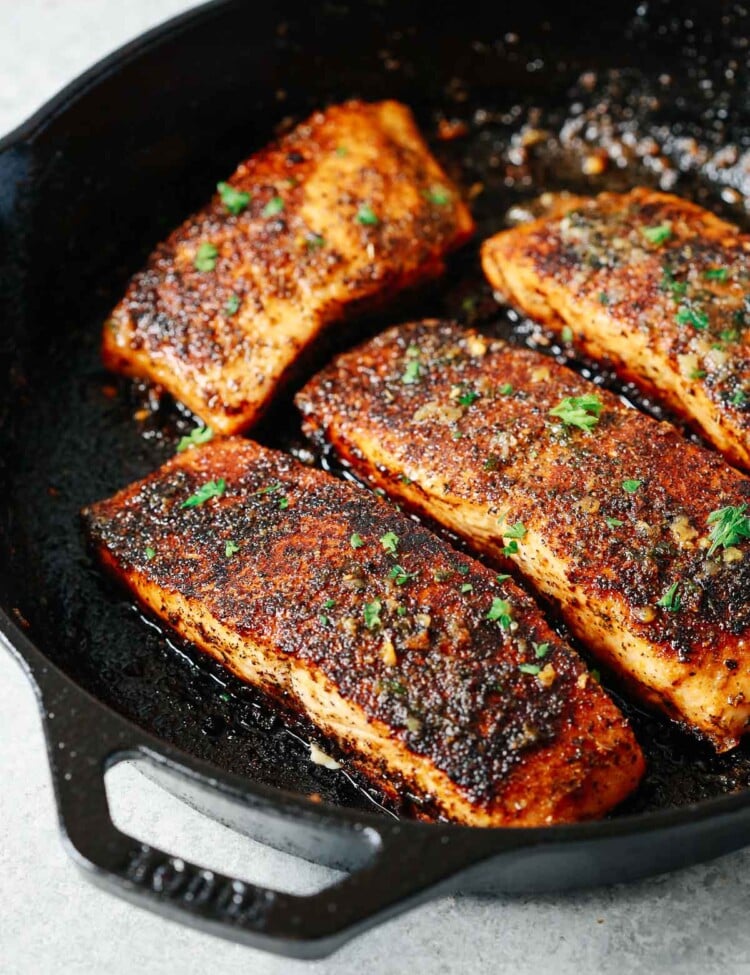 four blackened salmon fillets in a cast iron skillet