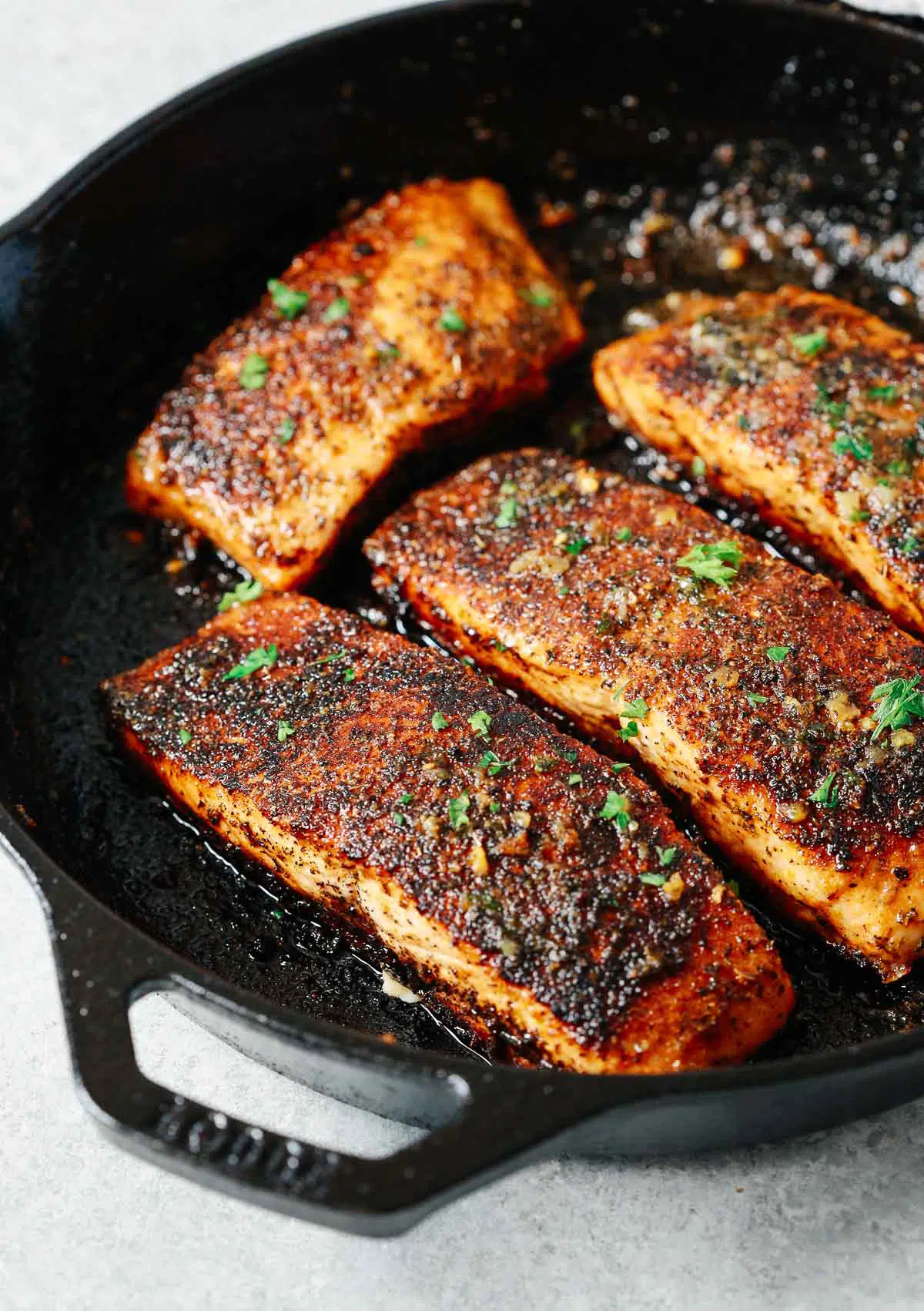 four blackened salmon fillets in a cast iron skillet