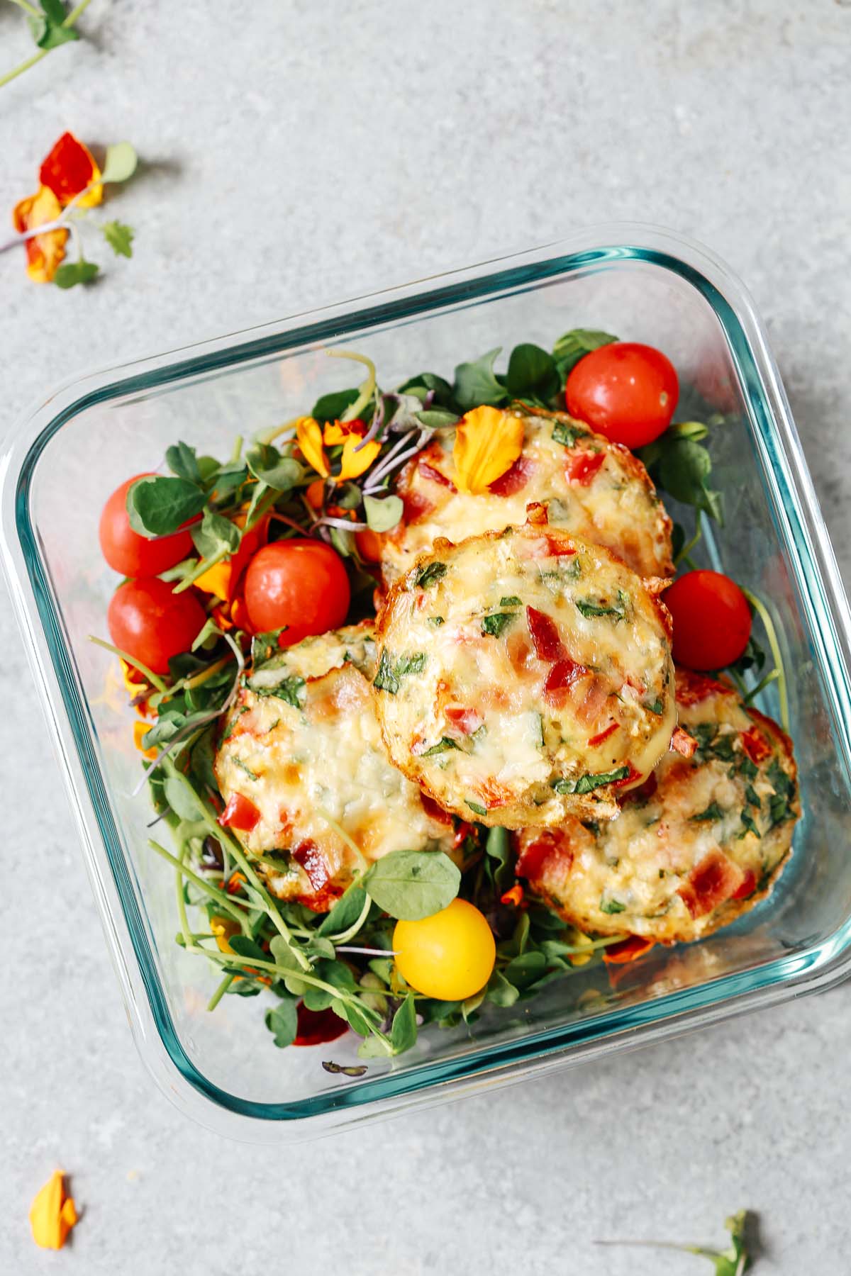 meal prep container with 3 breakfast egg muffins and cherry tomatoes on top of salad greens