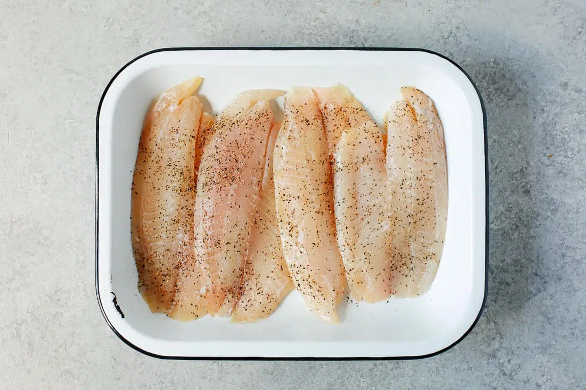 rectangle baking dish on a counter with tilapia fillets covered in salt and pepper