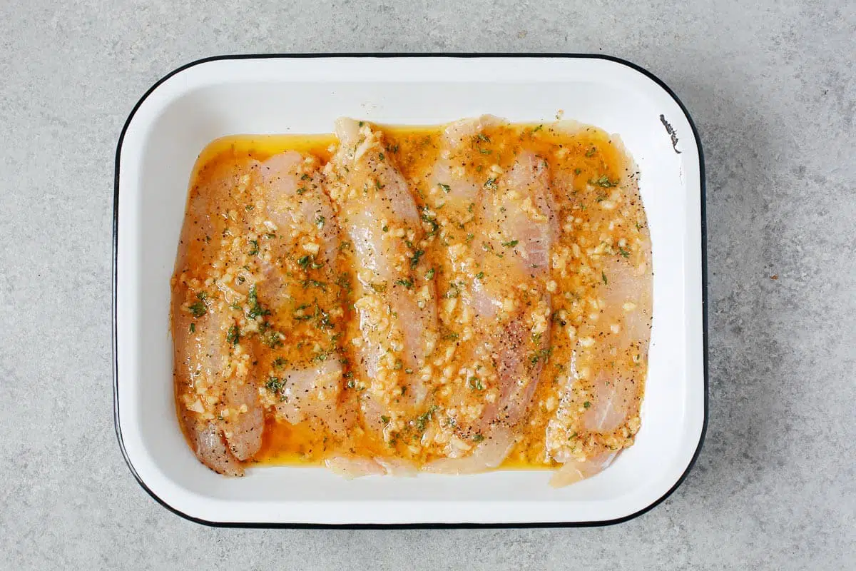 white fish covered in garlic butter sauce inside a baking dish