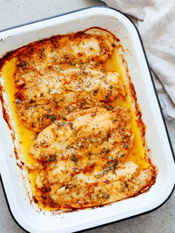 cooked tilapia fillets with garlic butter sauce in a white baking dish