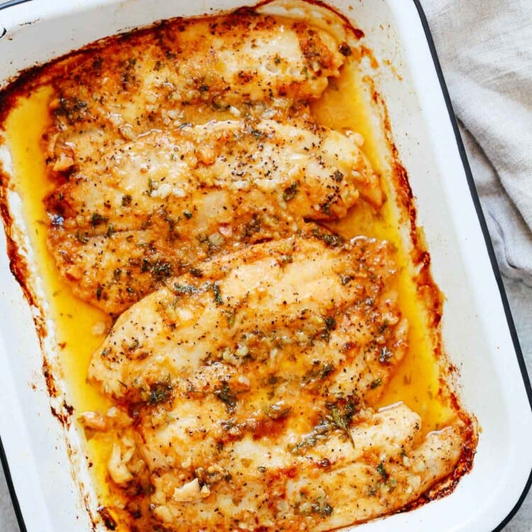 cooked tilapia fillets with garlic butter sauce in a white baking dish