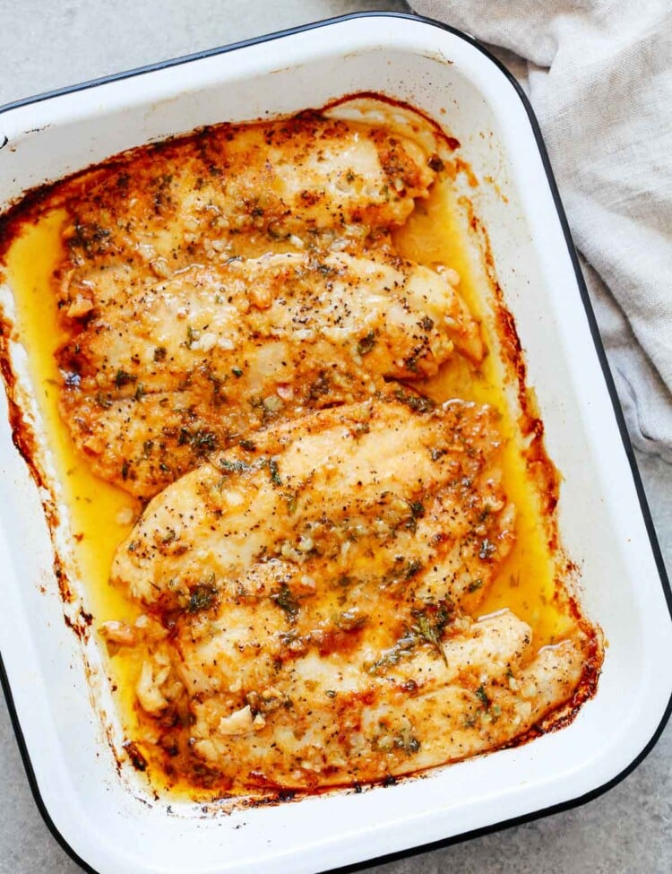 cooked tilapia fillets with garlic butter sauce in a white baking dish