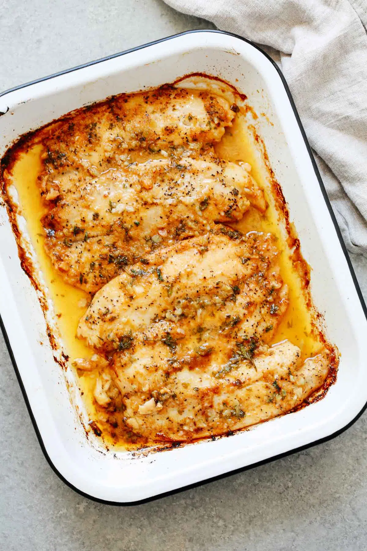 cooked tilapia fillets with garlic butter sauce in a white baking dish