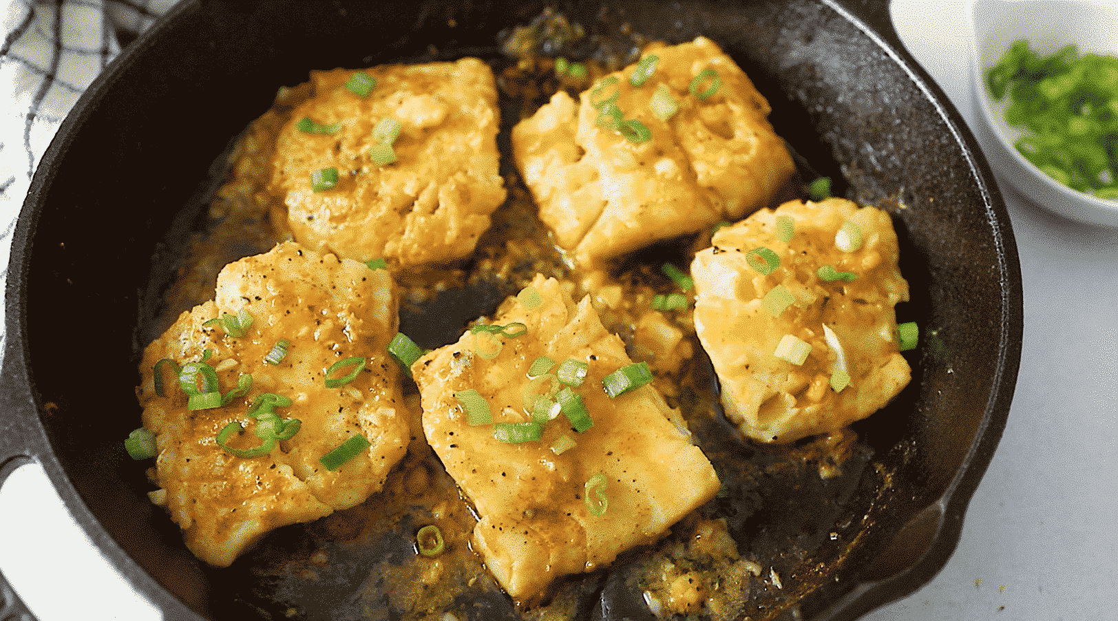 Close up of five garlic butter cods in a cast iron pan.