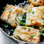 close up of white fish fillets garnished with scallions cooking in cast iron skillet