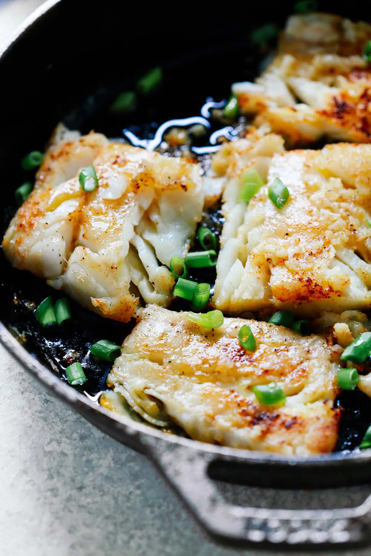 close up of white fish fillets garnished with scallions cooking in cast iron skillet 
