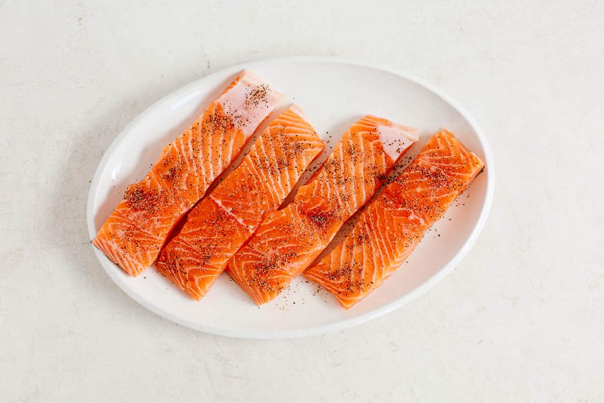 overhead image: four raw salmon fillets on a white platter for a pan seared salmon recipe