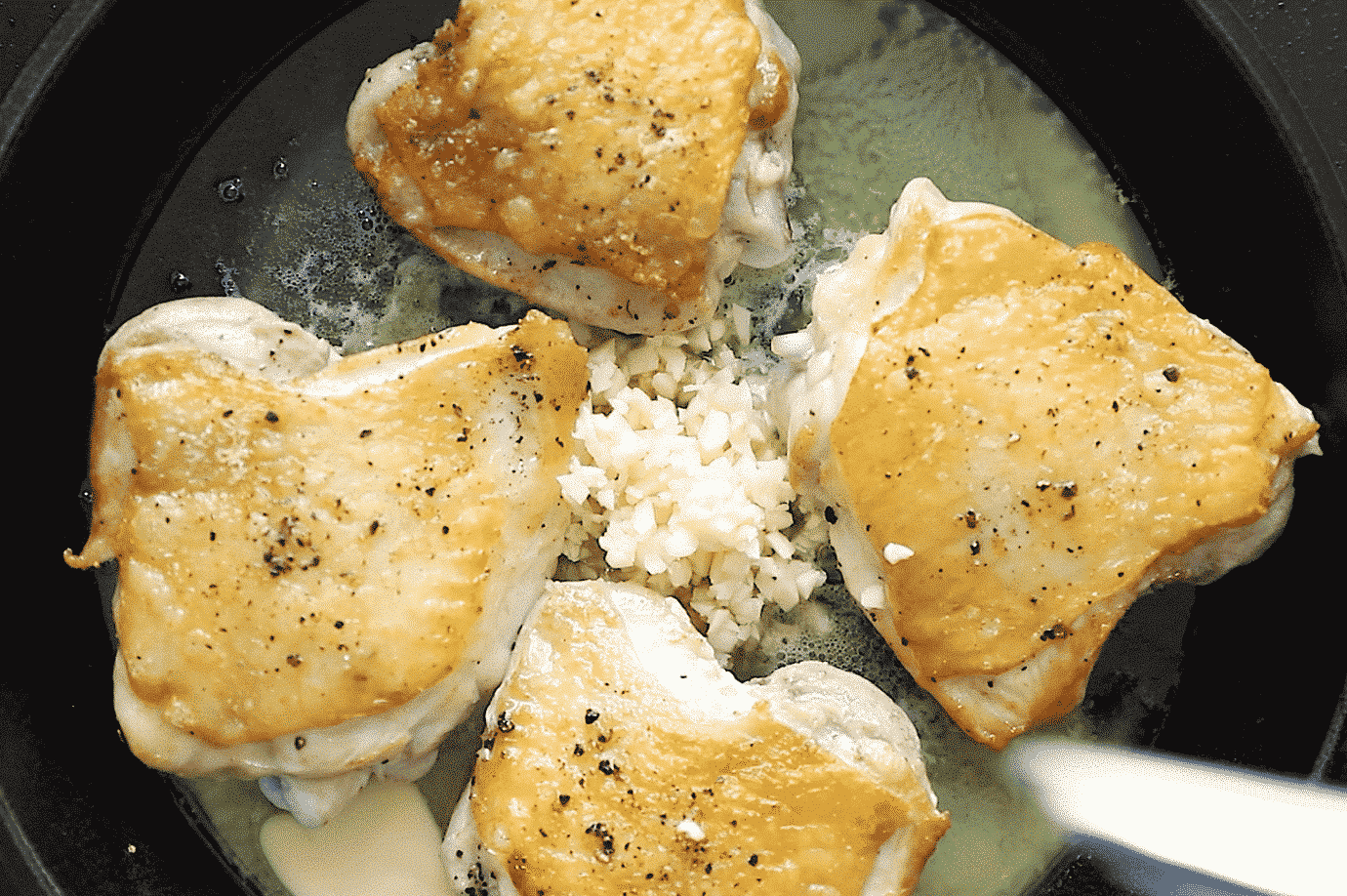 overhead view of Chicken Thighs with crispy skin in a cast iron skillet with butter and garlic