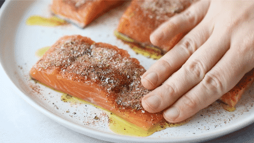 A close up of salmon fillets being with dried spices on top