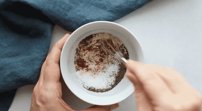 A hand whisks a mixture of spices and salt in a small white bowl for a blackened salmon recipe.