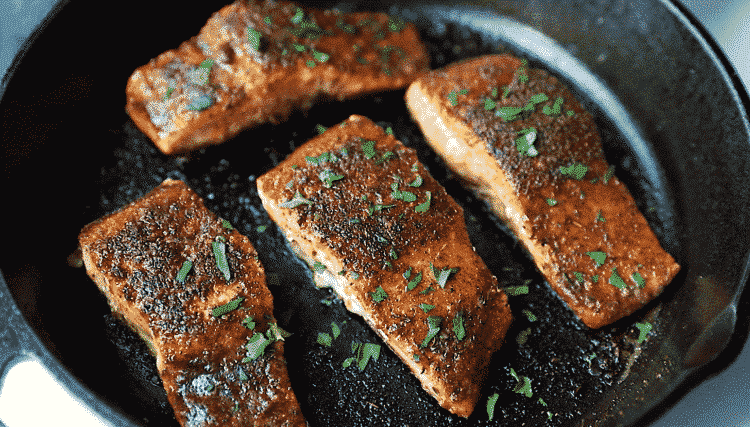 overhead view of a cast iron skillet containing blackened salmon