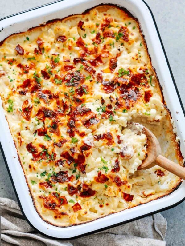close up of a cauliflower casserole in a baking dish with a wooden spoon scooping.