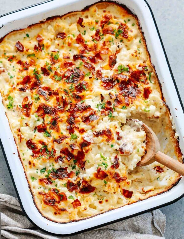 close up of a cauliflower casserole in a baking dish with a wooden spoon scooping.