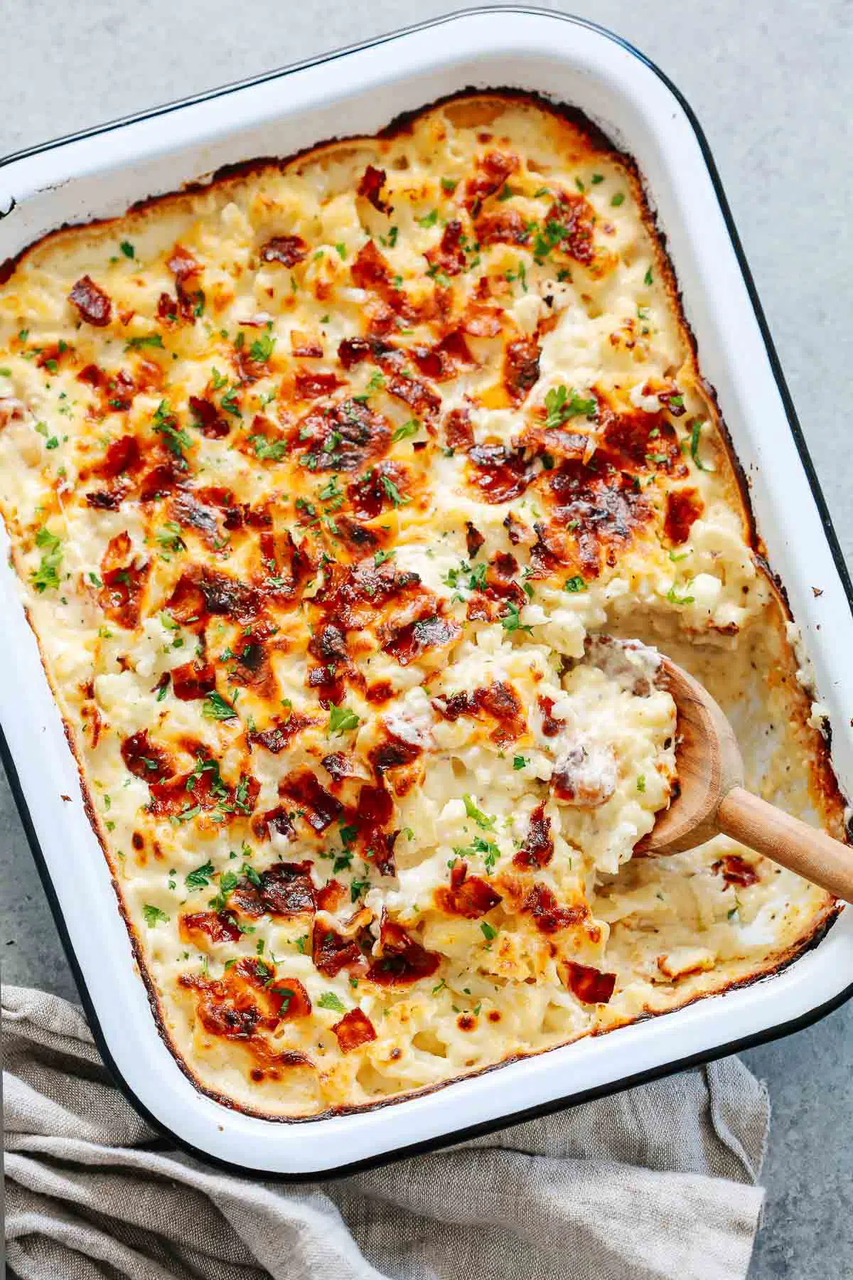 close up of a cauliflower casserole in a baking dish with a wooden spoon scooping. 