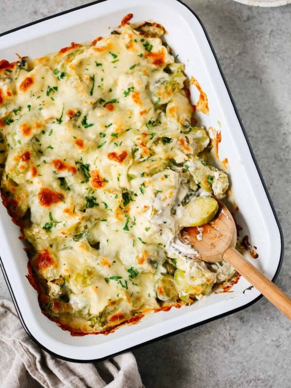 Brussels sprouts casserole recipe in a baking dish with a wooden spoon inside.