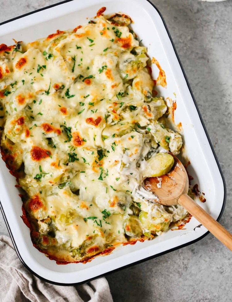 Brussels sprouts casserole recipe in a baking dish with a wooden spoon inside.