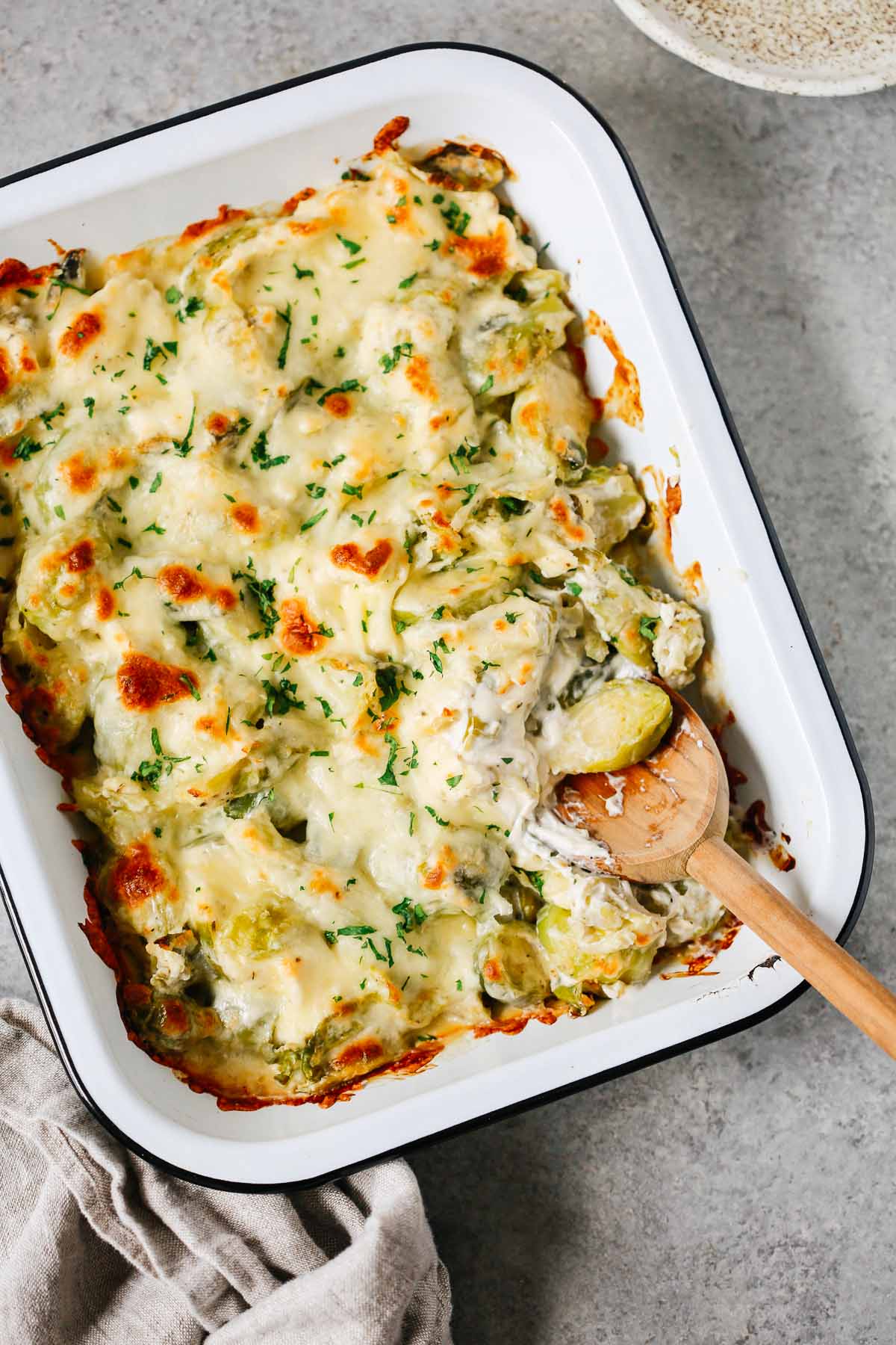 Brussels sprouts casserole recipe in a baking dish with a wooden spoon inside.