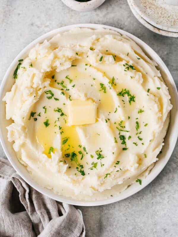 overhead view of a creamy mashed potatoes in a white bowl with butter on top.