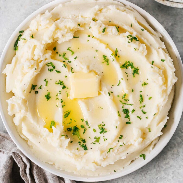 overhead view of a creamy mashed potatoes in a white bowl with butter on top.