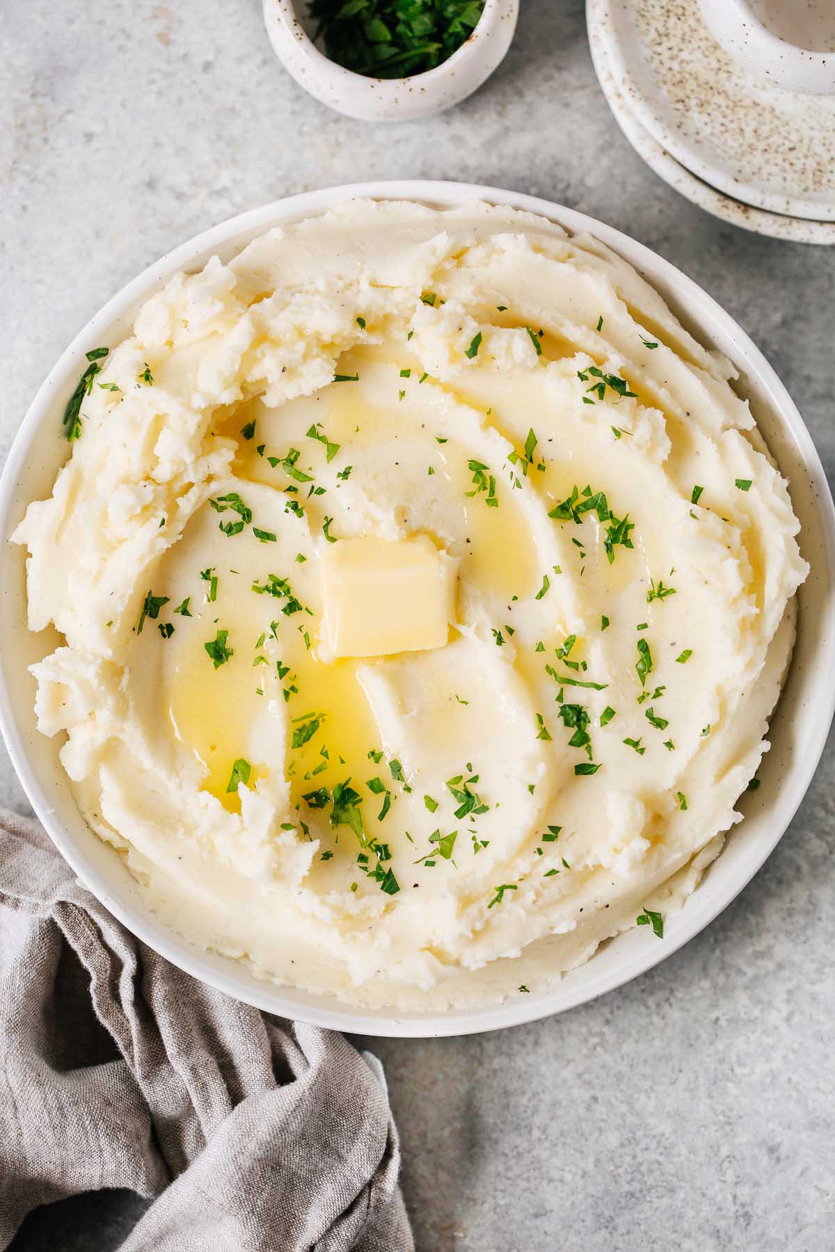overhead view of a creamy mashed potatoes in a white bowl with butter on top. 
