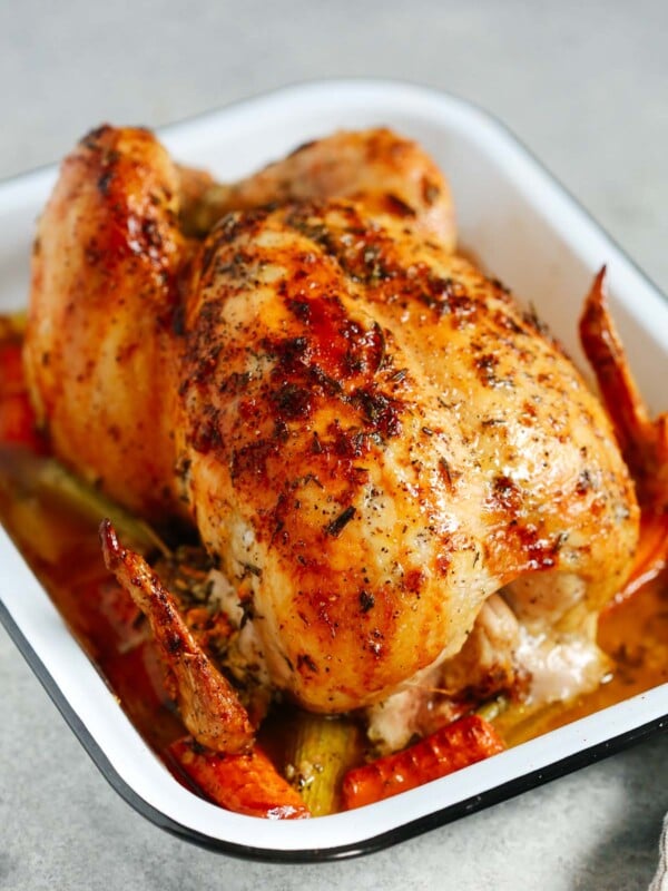 Photo of a garlic herb butter roast chicken inside of a white roasting pan.