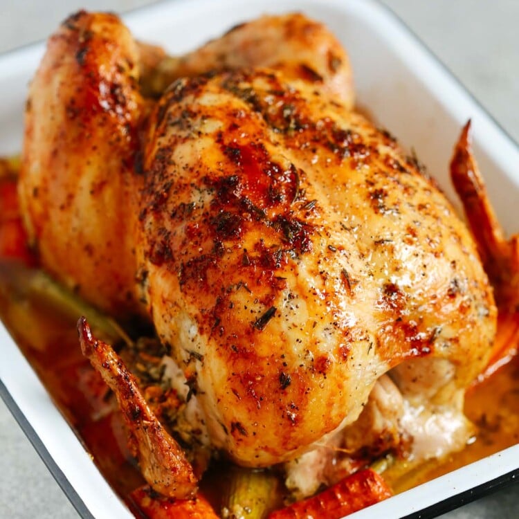 Photo of a garlic herb butter roast chicken inside of a white roasting pan.