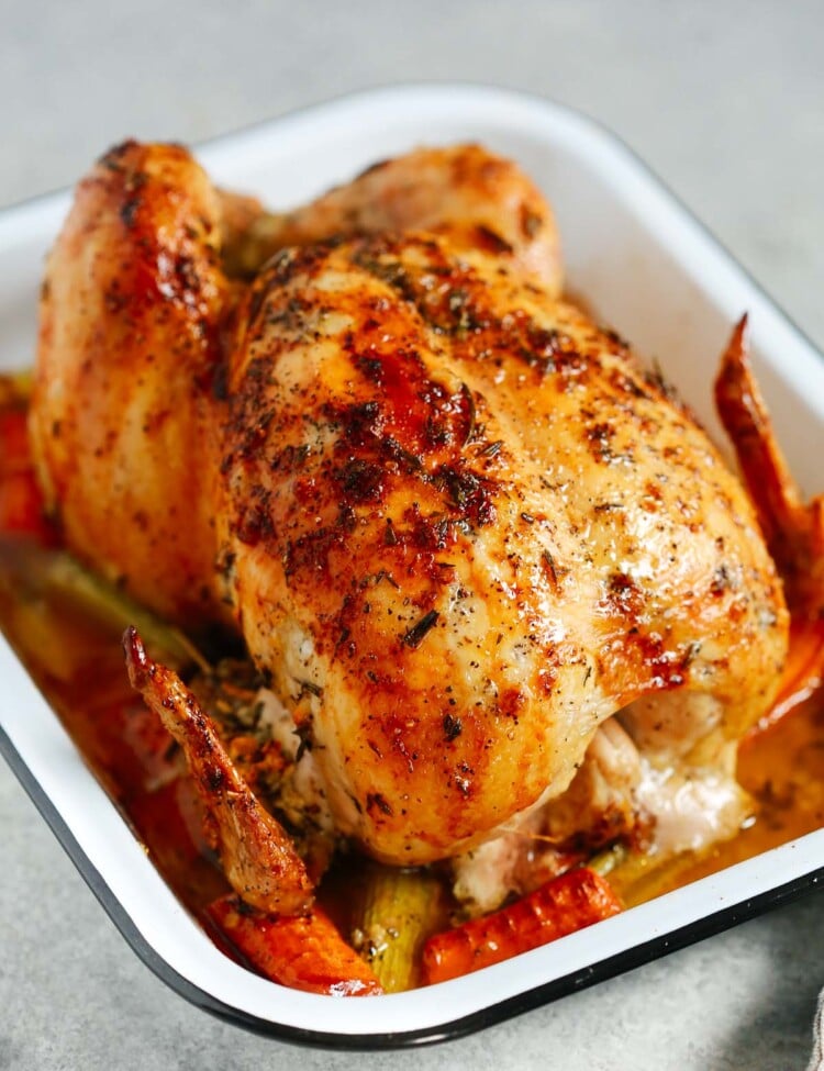 Photo of a garlic herb butter roast chicken inside of a white roasting pan.