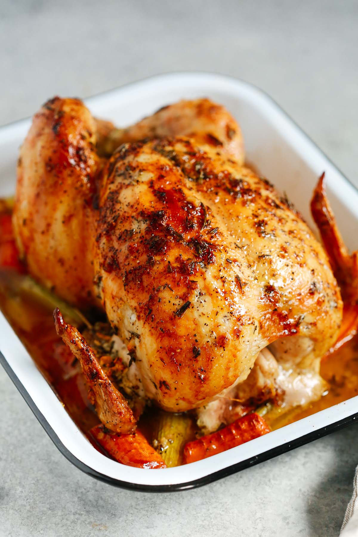 Photo of a roasted whole chicken inside of a white roasting pan.