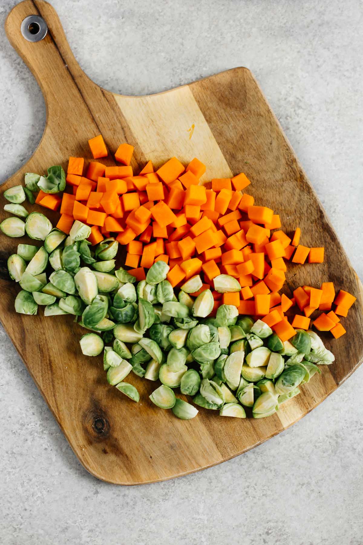 Overhead image of a cutting board with diced butternut squash and quartered Brussels sprouts. 