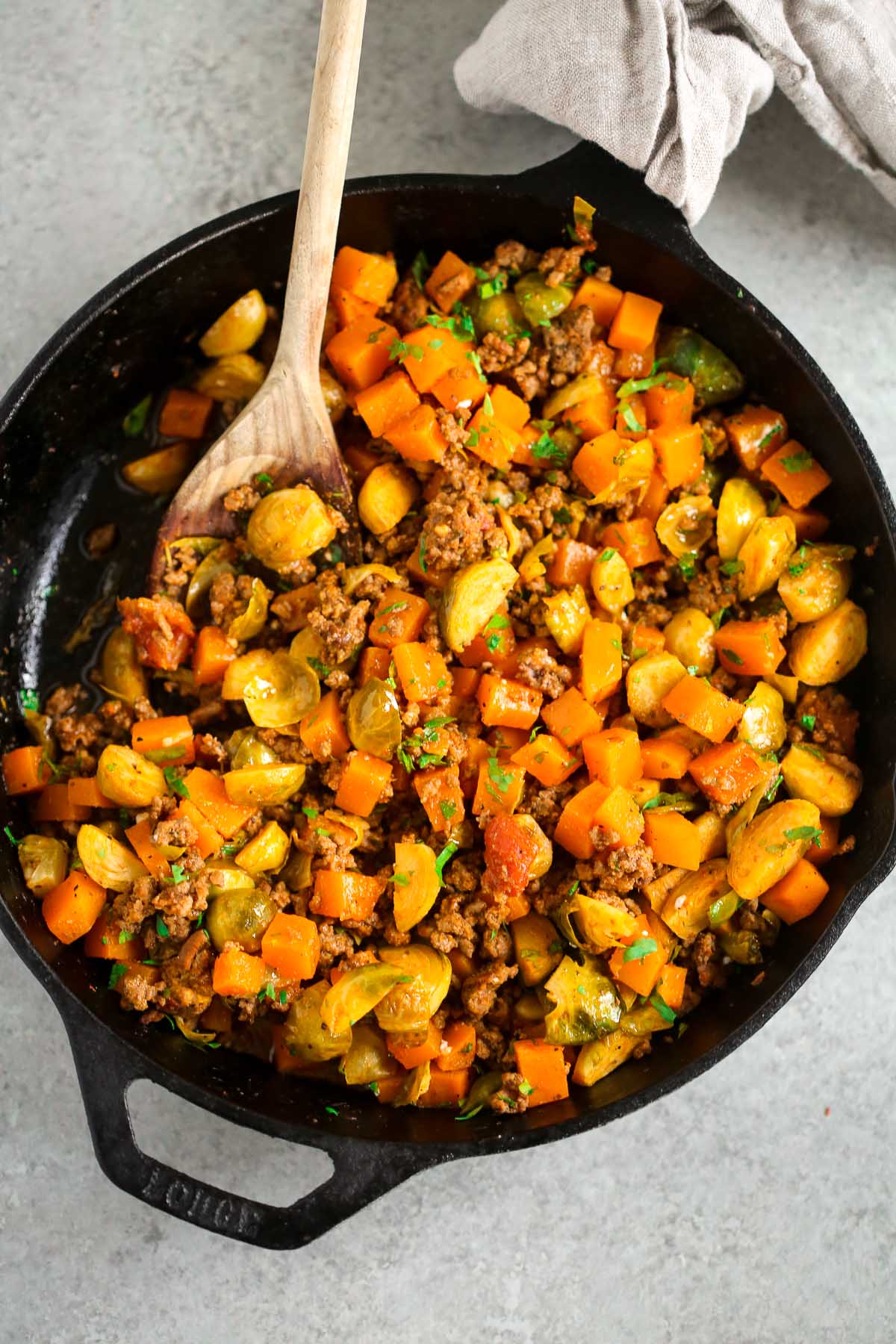 A cast iron skillet with ground beef with butternut squash with a wooden spoon scooping.