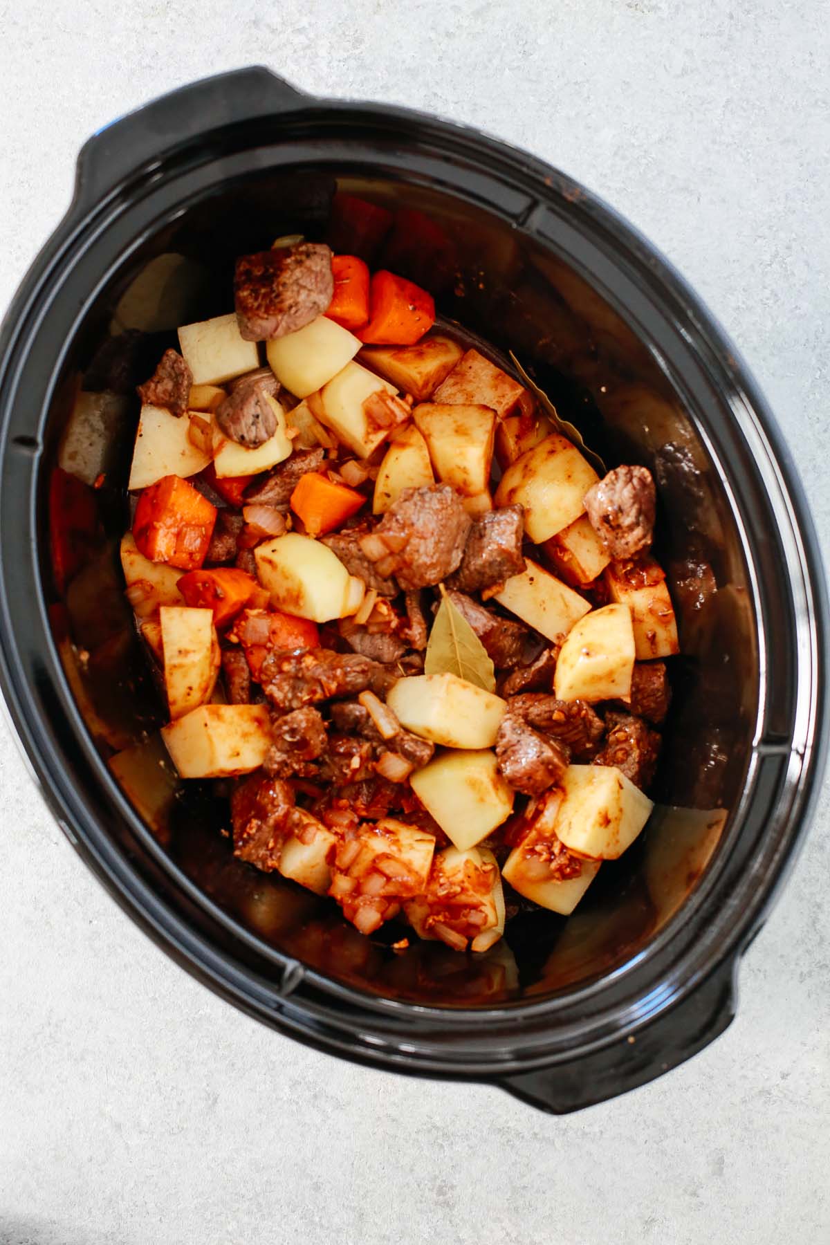 Overhead image of ingredients for the beef stew being adding to the slow cooker before cooking.