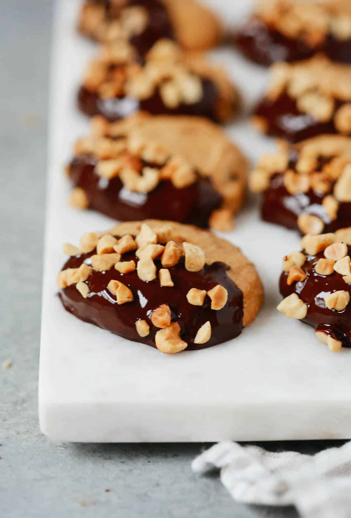 Multiple low-carb peanut butter cookies dipped in chocolate and topped with chopped peanuts. 
