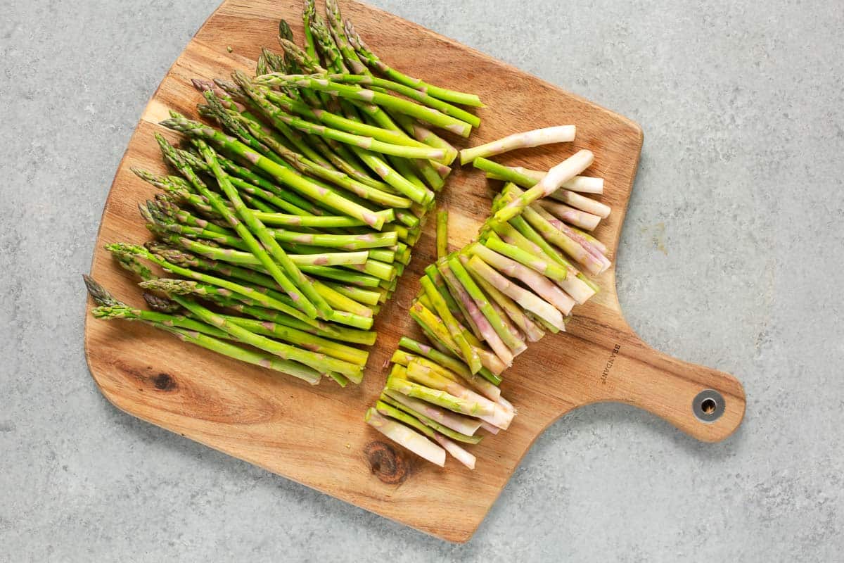Cutting off the woody ends of asparagus spears on a cutting board.