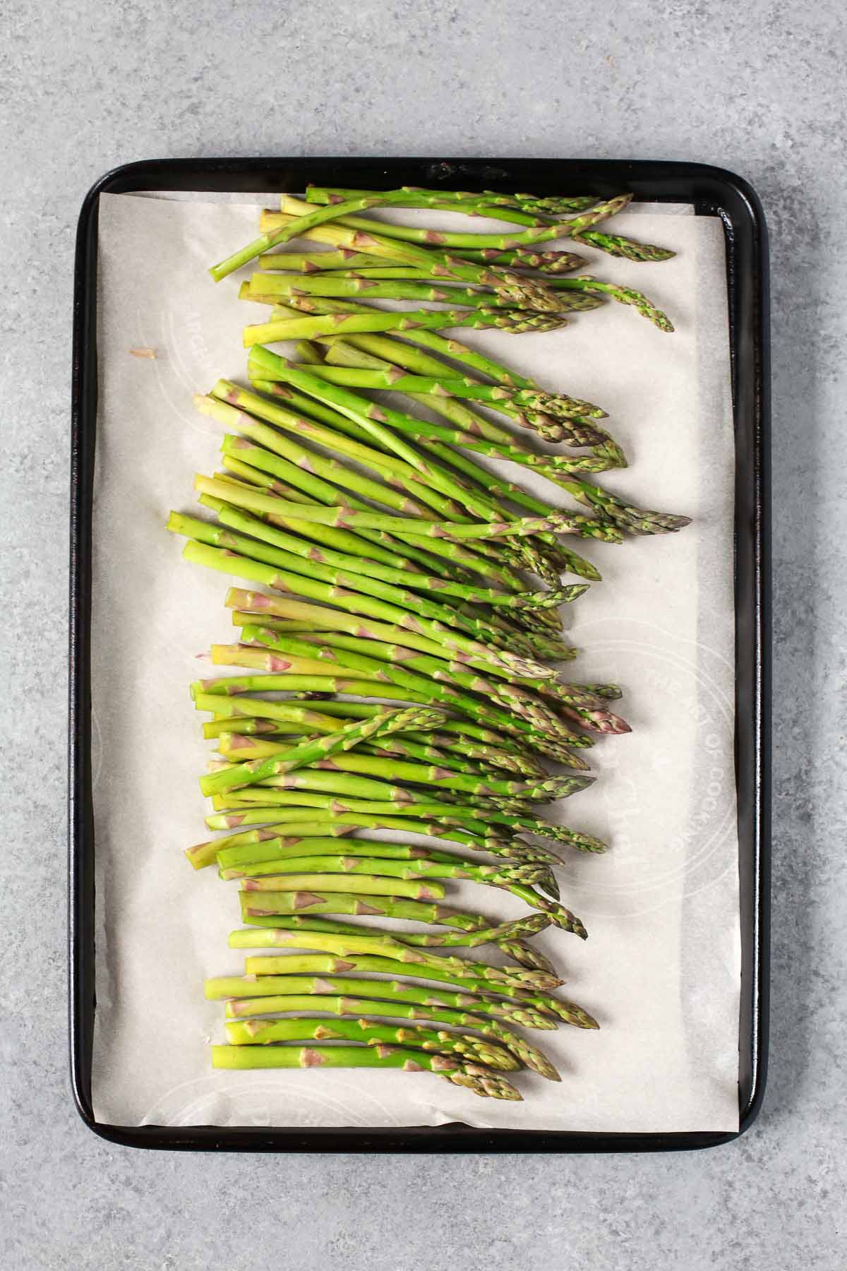 Placing prepared asparagus onto a sheet pan lined with parchment paper.