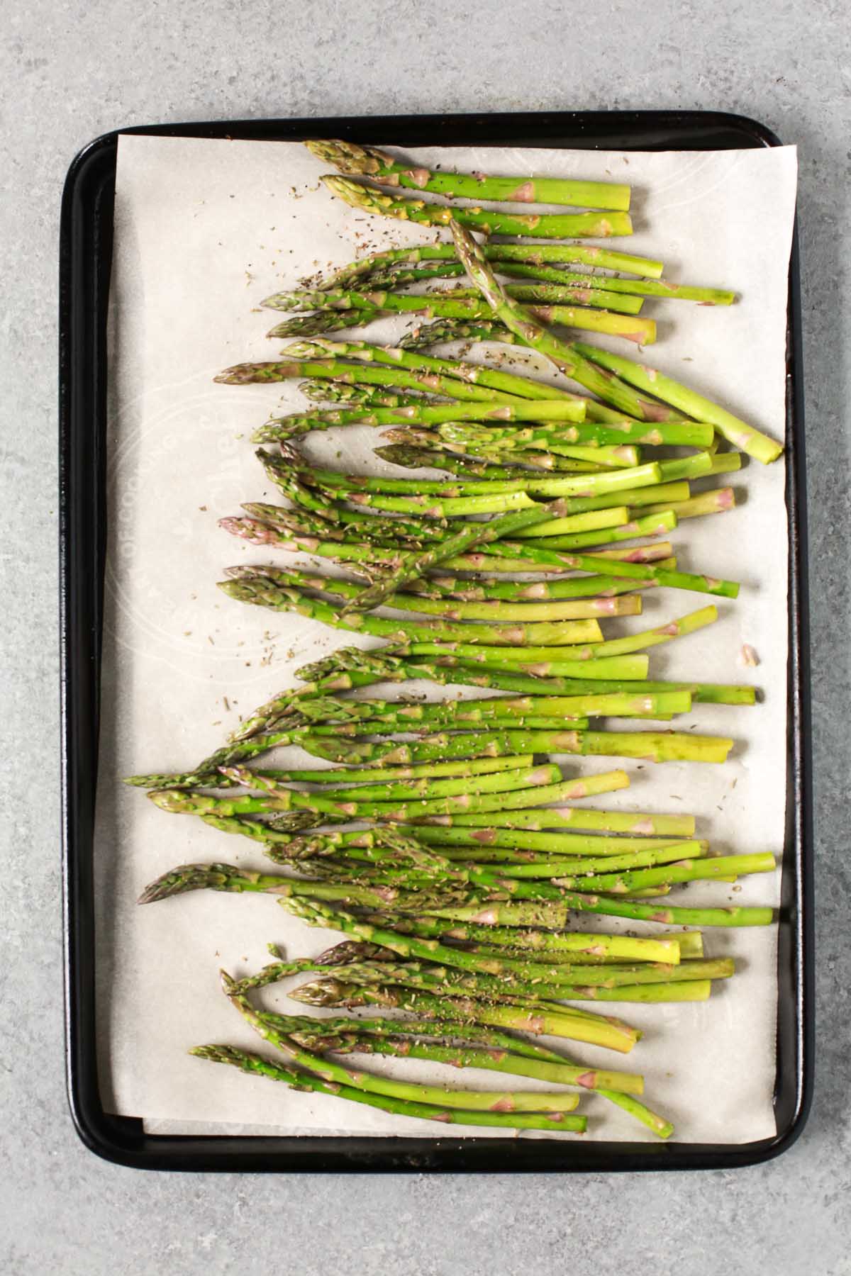 Seasoning asparagus on a sheet pan before roasting.