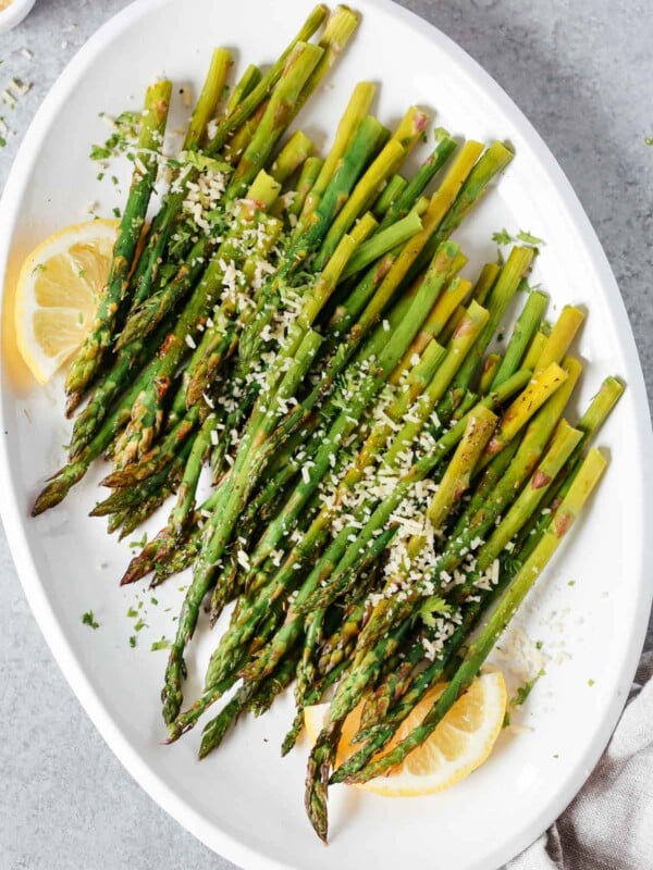 Easy roasted asparagus on a serving platter topped with parmesan cheese and lemon wedges.